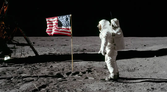Buzz Aldrin walking on the surface of the Moon next to an American flag